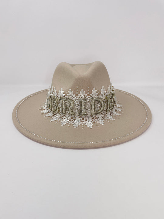 Beige fedora hat featuring interchangeable handmade lace bands with Velcro attachments. Includes three designs: “BRIDE” and “WIFEY” lettering embellished with crystals and pearls, and an elegant floral motif with lace, handmade  flowers and beaded details. A stylish 3-in-1 bridal accessory made in the UK. One size, wide brim fedora, luxury fedora, bride hat, wifey hat, floral hat, hen do