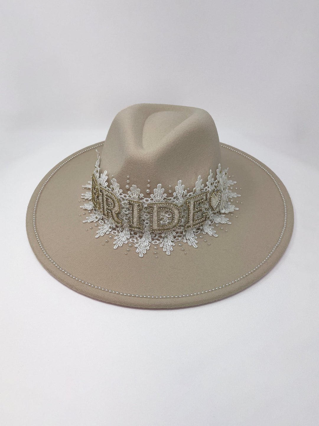 Beige fedora hat featuring interchangeable handmade lace bands with Velcro attachments. Includes three designs: “BRIDE” and “WIFEY” lettering embellished with crystals and pearls, and an elegant floral motif with lace, handmade  flowers and beaded details. A stylish 3-in-1 bridal accessory made in the UK. One size, wide brim fedora, luxury fedora, bride hat, wifey hat, floral hat, hen do