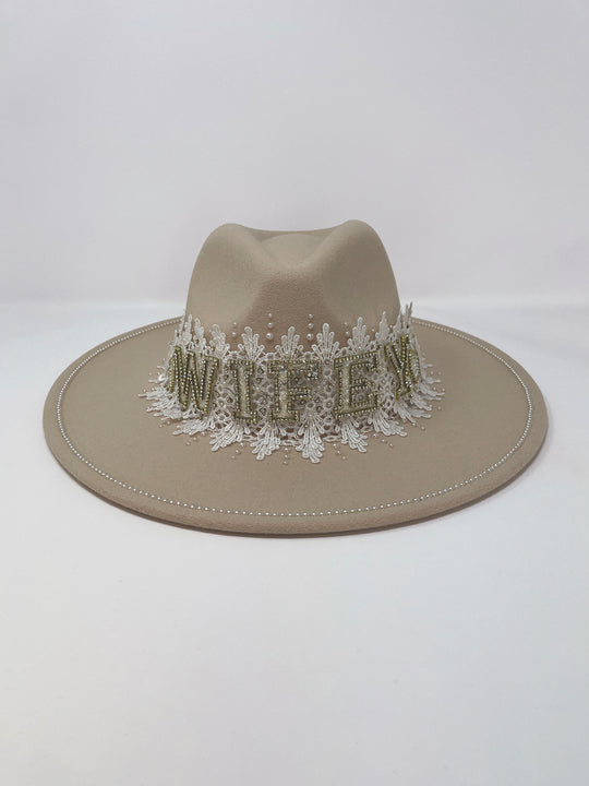 Beige fedora hat featuring interchangeable handmade lace bands with Velcro attachments. Includes three designs: “BRIDE” and “WIFEY” lettering embellished with crystals and pearls, and an elegant floral motif with lace, handmade  flowers and beaded details. A stylish 3-in-1 bridal accessory made in the UK. One size, wide brim fedora, luxury fedora, bride hat, wifey hat, floral hat, hen do