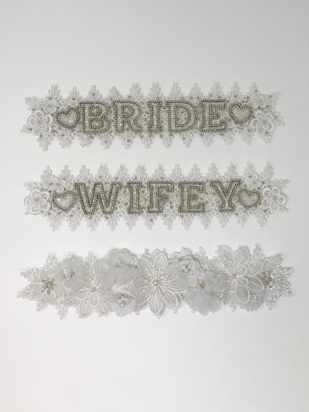 Beige fedora hat featuring interchangeable handmade lace bands with Velcro attachments. Includes three designs: “BRIDE” and “WIFEY” lettering embellished with crystals and pearls, and an elegant floral motif with lace, handmade  flowers and beaded details. A stylish 3-in-1 bridal accessory made in the UK. One size, wide brim fedora, luxury fedora, bride hat, wifey hat, floral hat, hen do